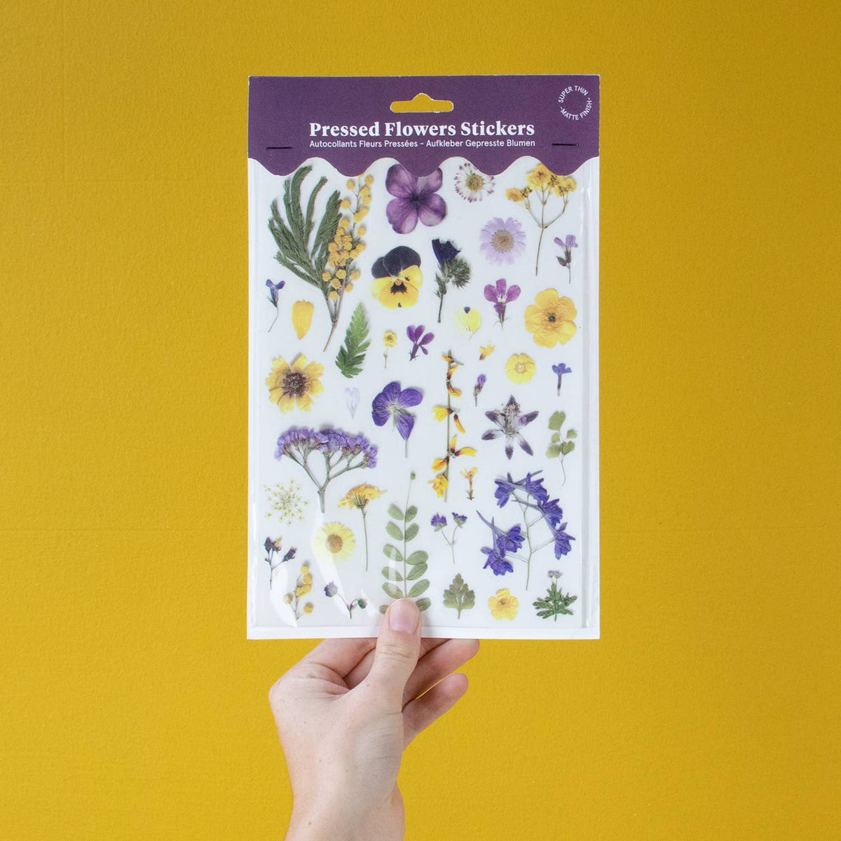 Sheet of pressed flowers stickers held by a hand against a yellow background