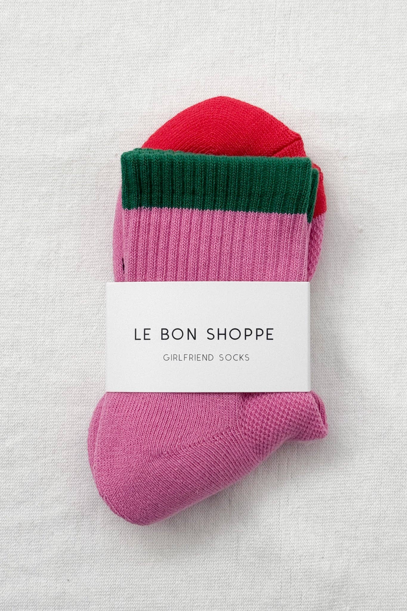 Pink and red sock with green trim on a textured white background, featuring 'Le Bon Shoppe' label.