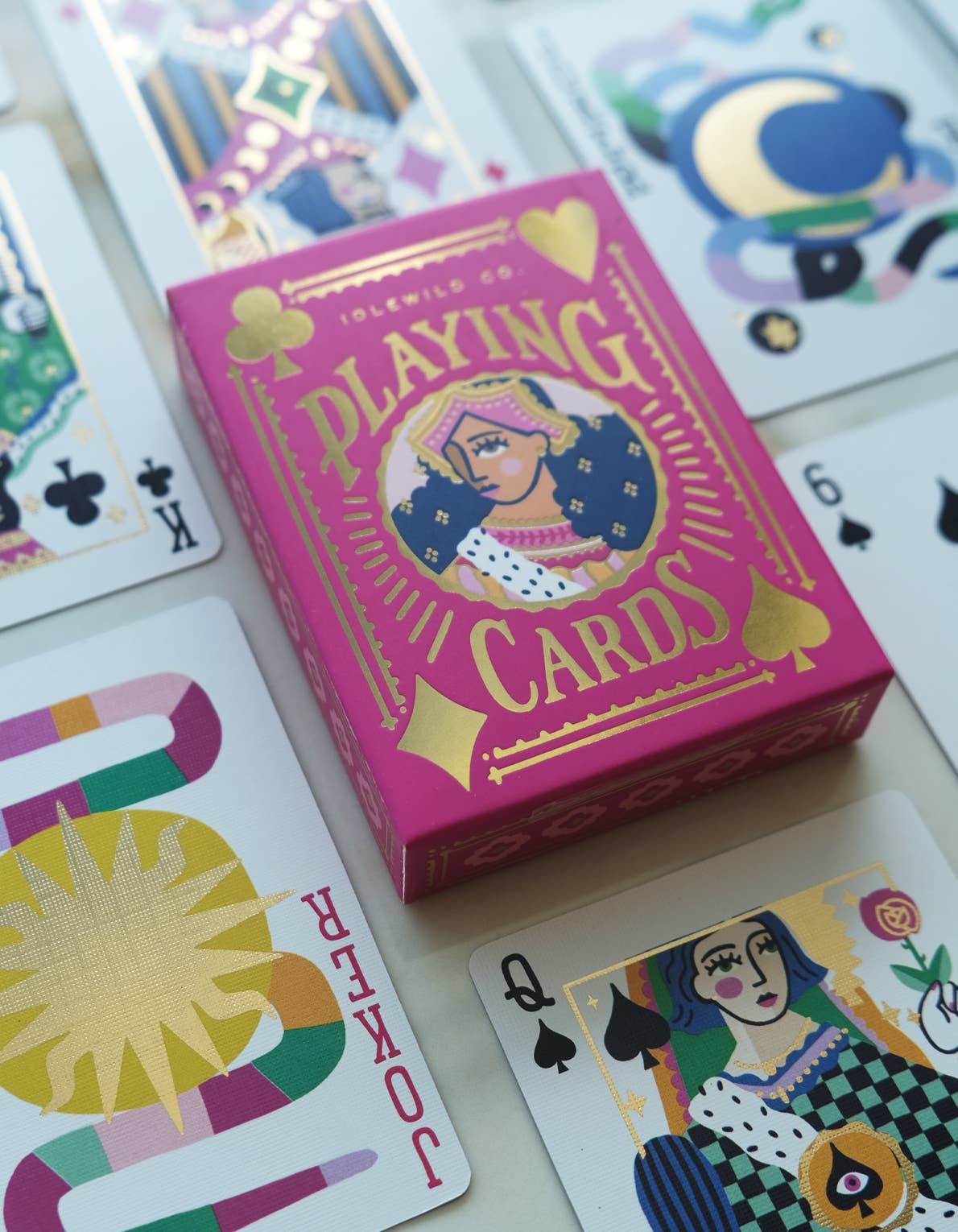 Pink deck of playing cards in a box with colorful designs on a wooden surface