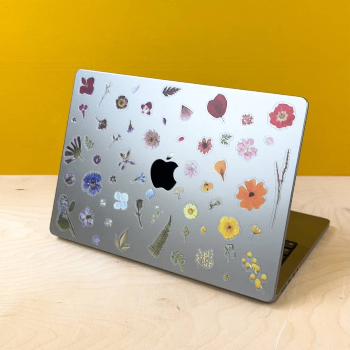 Laptop with floral stickers on a wooden surface against a yellow wall