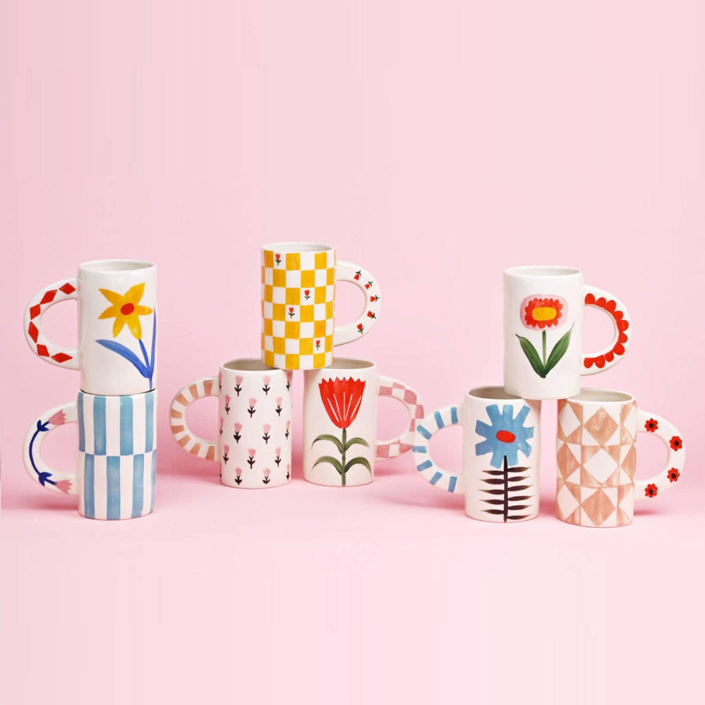 Set of colorful mugs with floral and geometric designs on a pink background