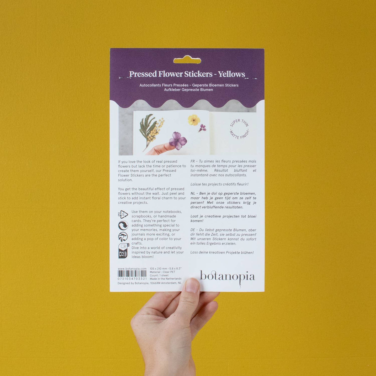Hand holding a package of pressed flower stickers with a yellow background