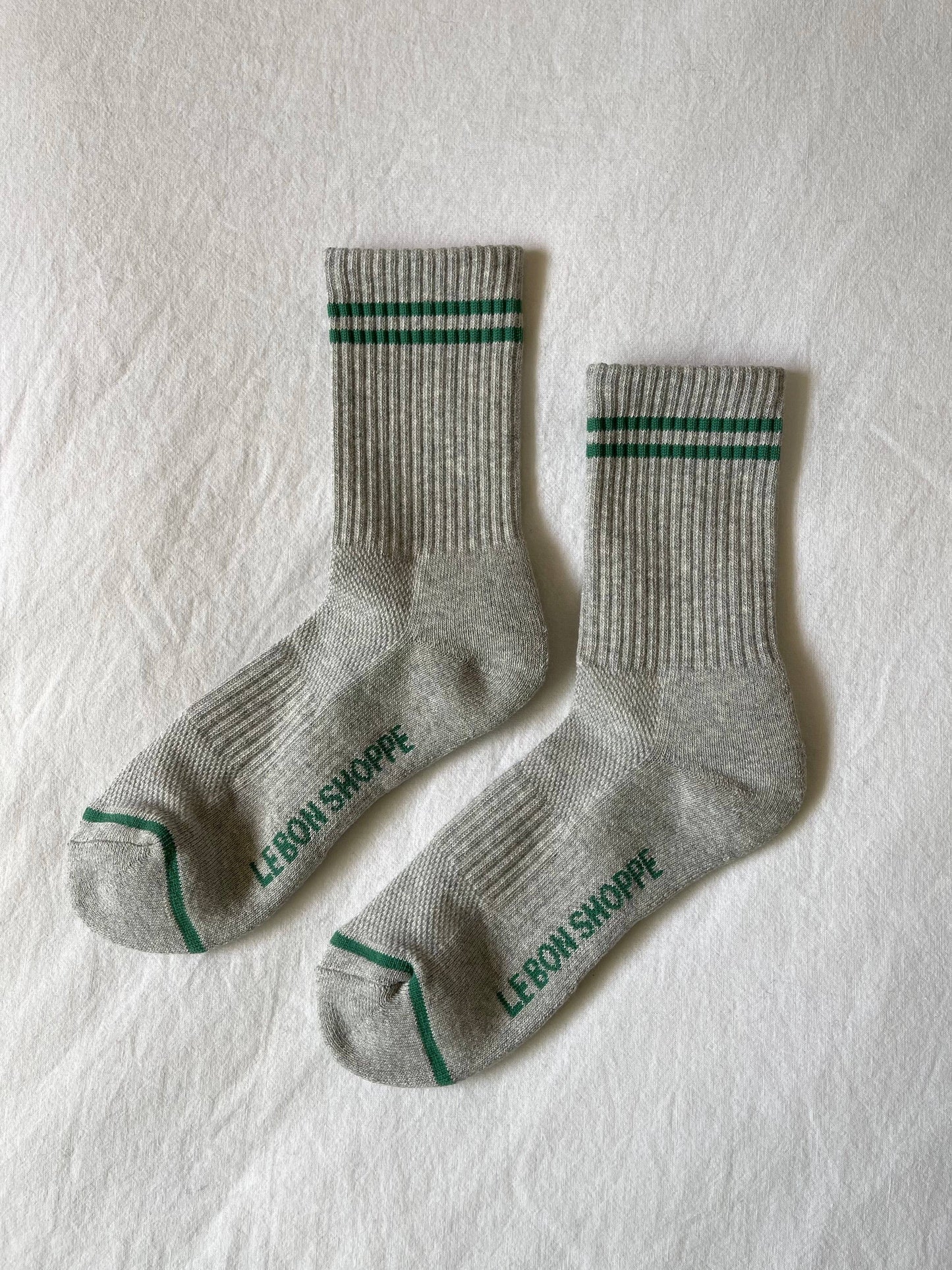 Two gray socks with green accents on a light textured surface