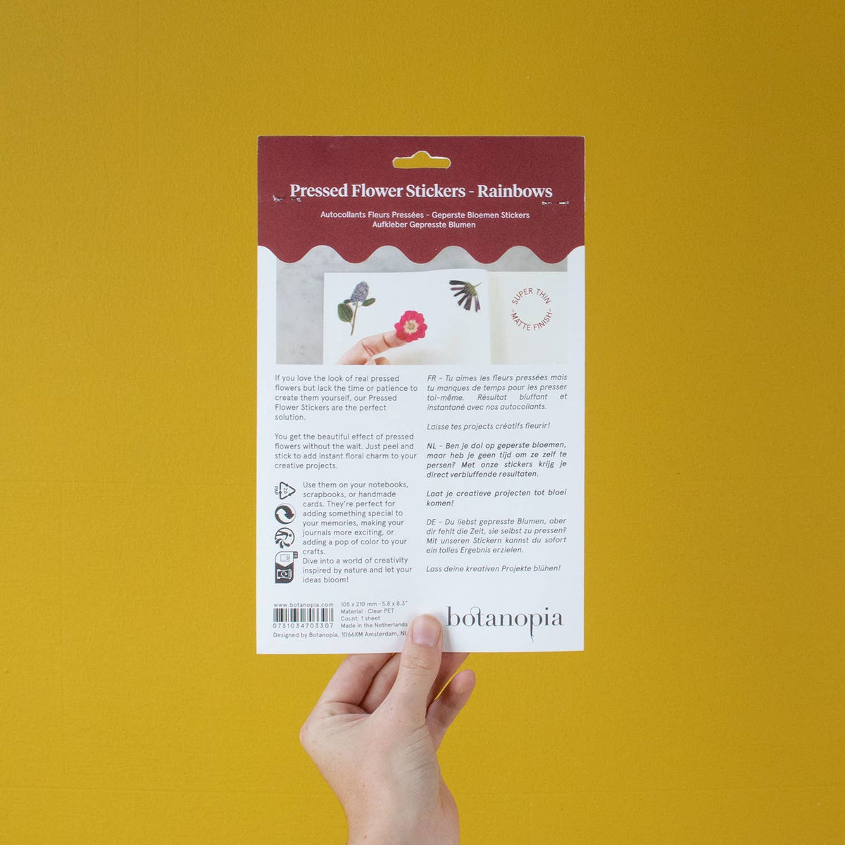 Hand holding a package of pressed flower stickers with Botanopia branding against a yellow background