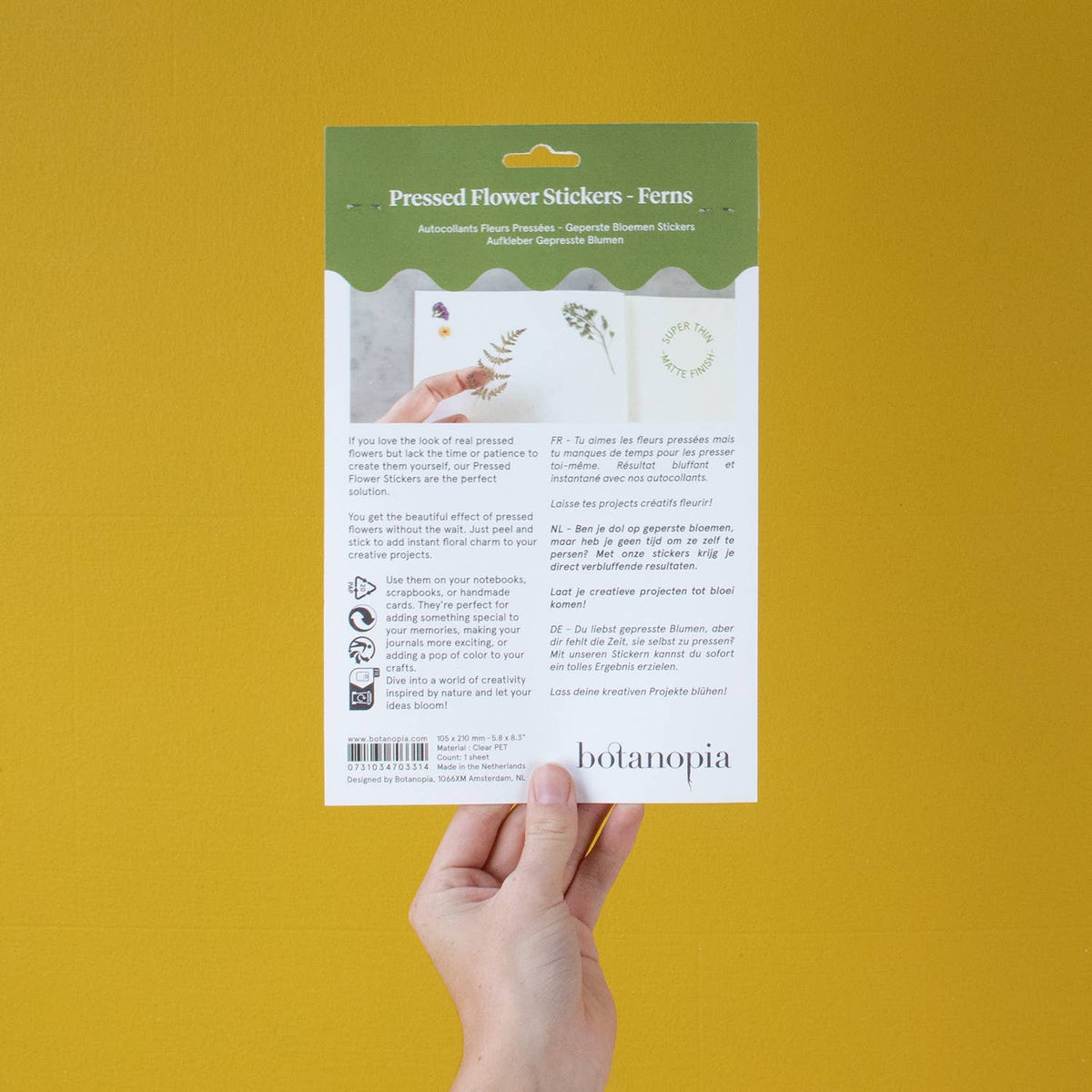 Hand holding a package of pressed flower stickers with Botanopia branding on a yellow background