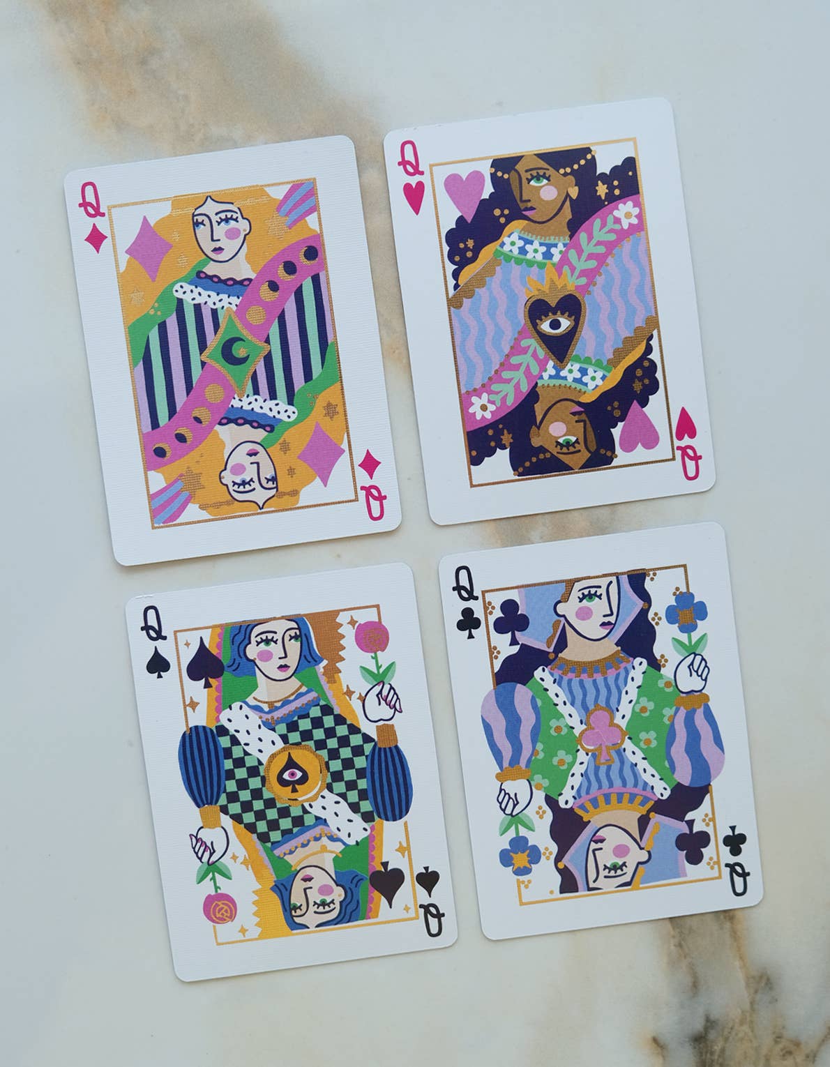 Four playing cards with colorful designs on a cream surface