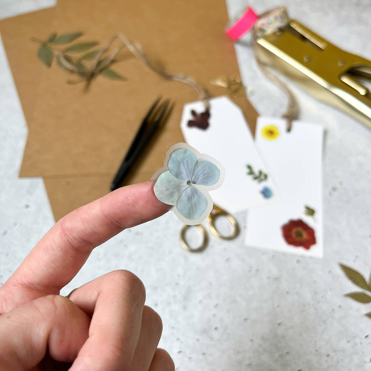 Hand holding a small floral sticker with craft supplies in the background