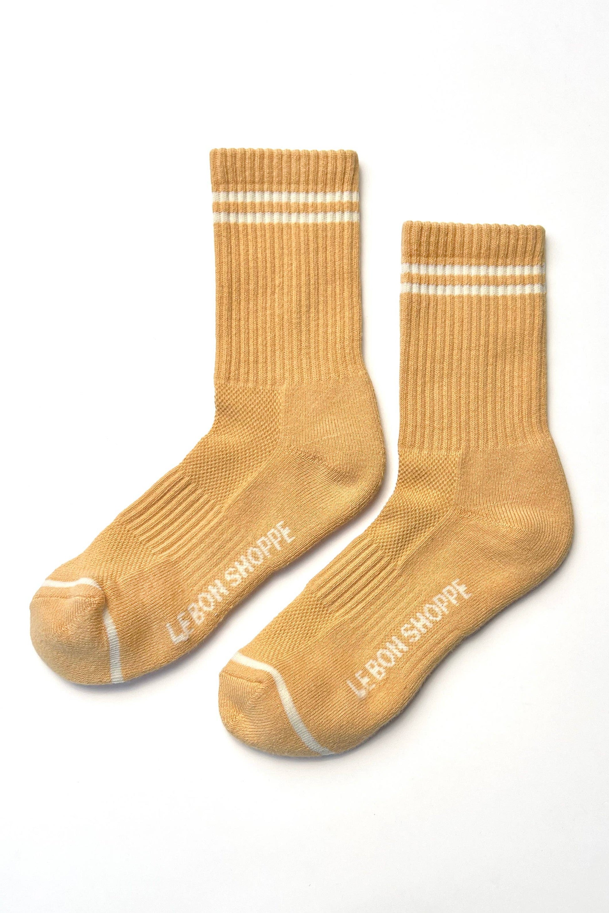 Pair of butter colored socks with white stripes and 'Le Bon Shoppe' branding on a white background