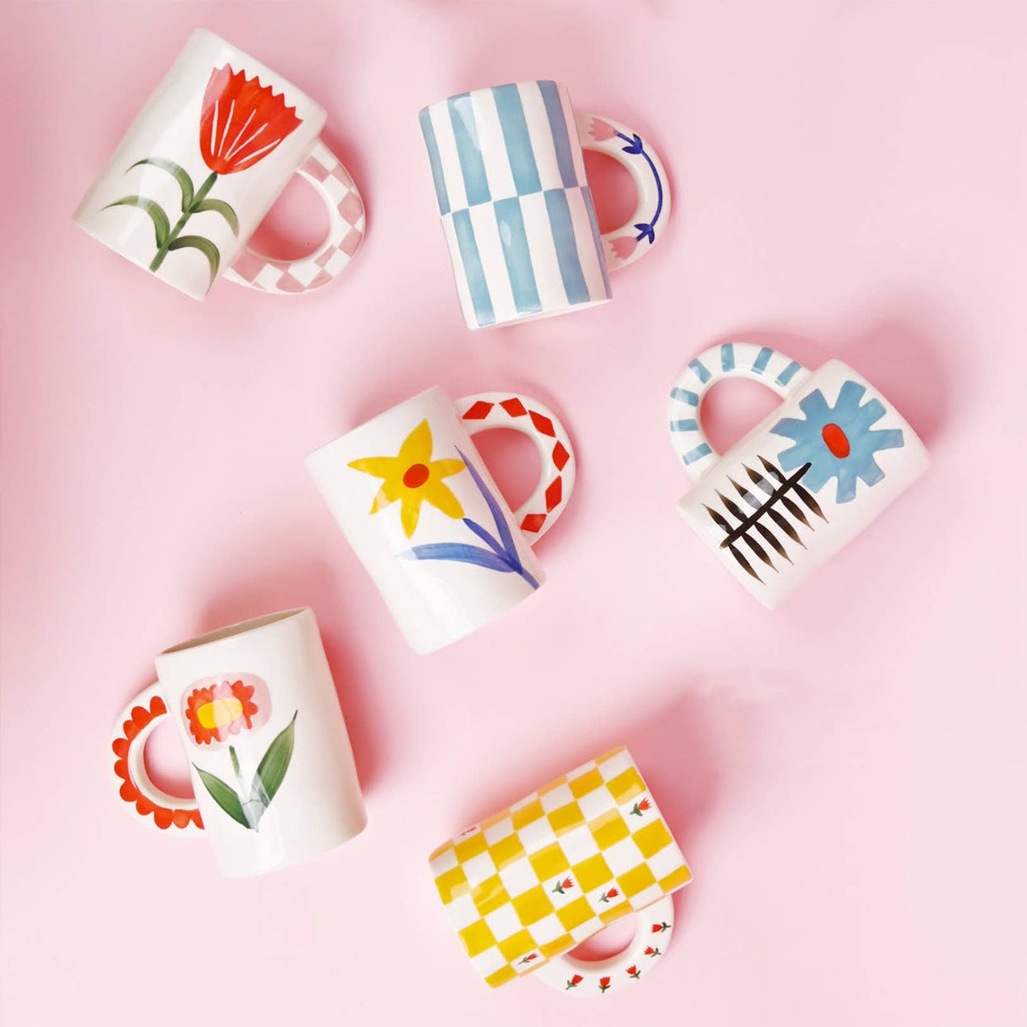 Set of colorful mugs with floral and abstract designs on a pink background