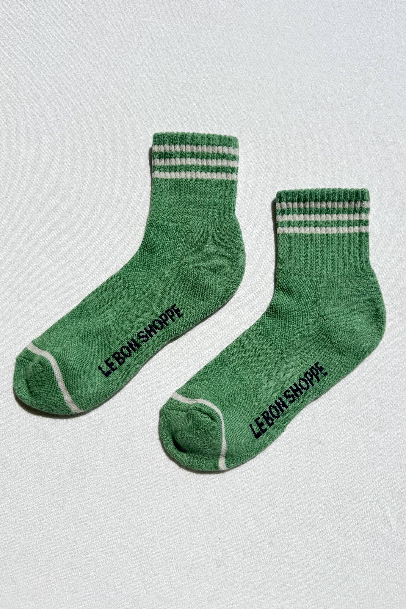 Green socks with white stripes and 'Le Bon Shoppe' branding on a light gray background