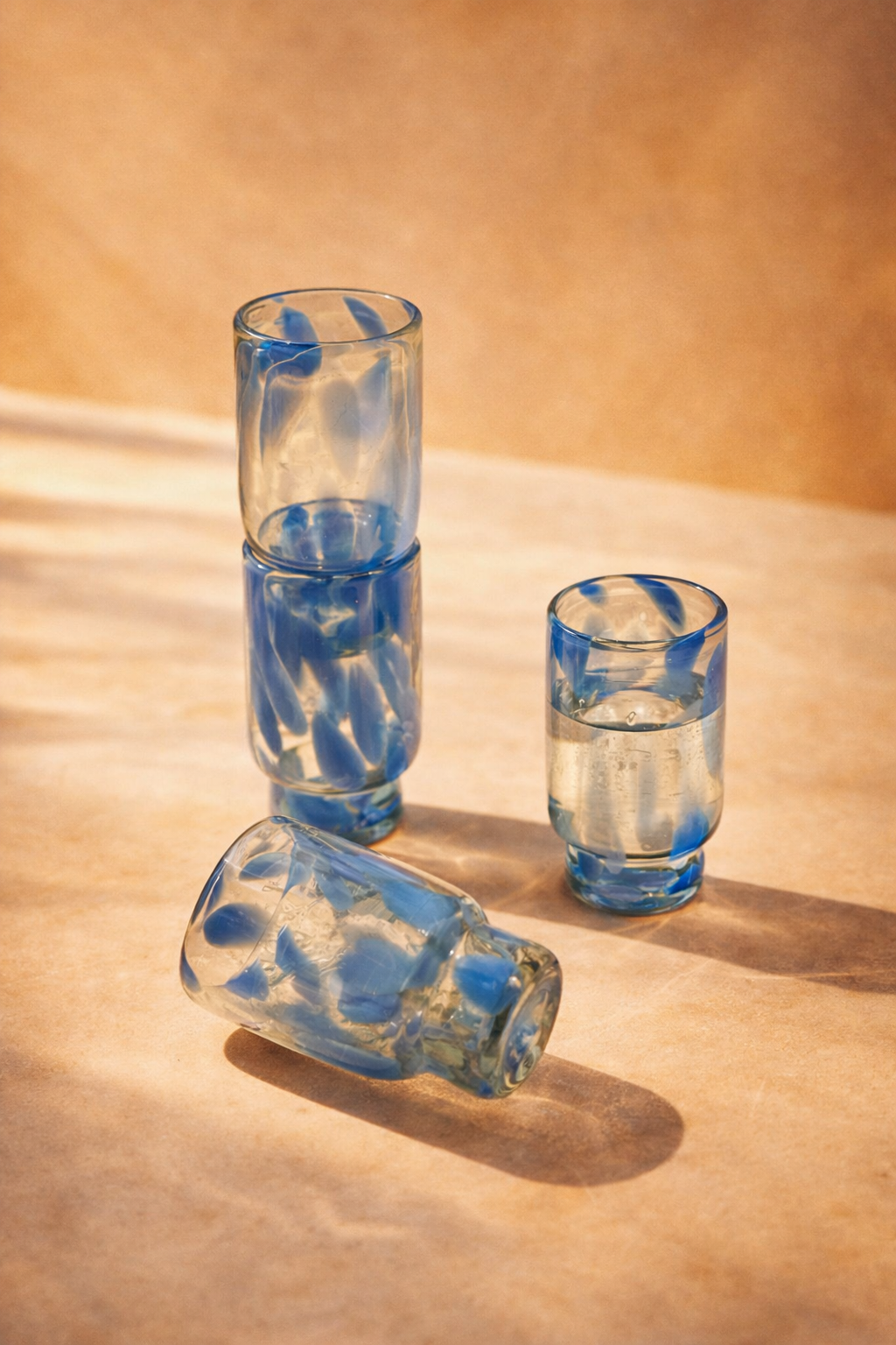 Set of four tall glasses in blue and clear recycled glass, arranged on a plain background.