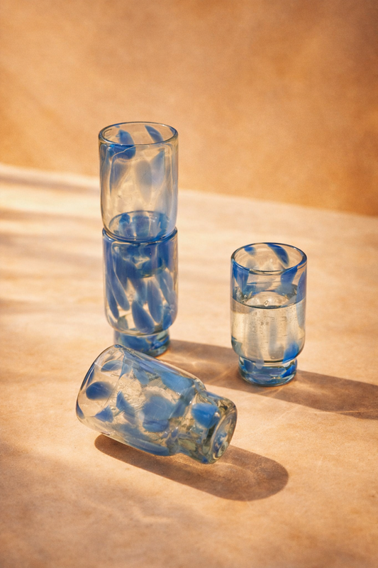 Set of four tall glasses in blue and clear recycled glass, arranged on a plain background.