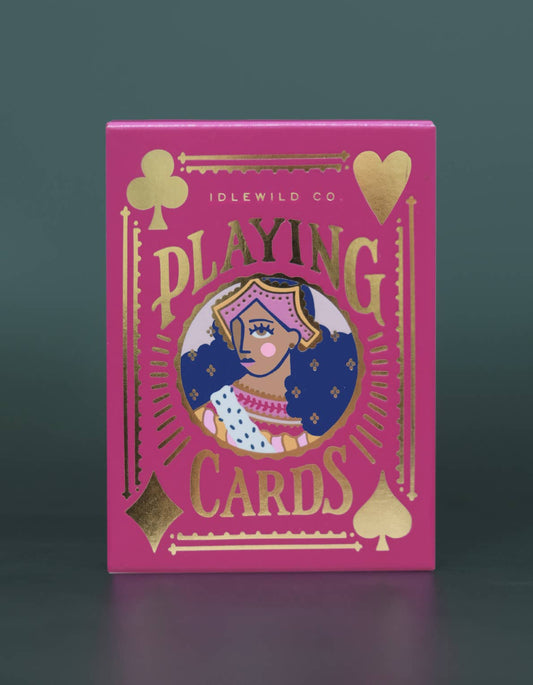 Pink playing card box with gold accents and a central illustration on a dark background