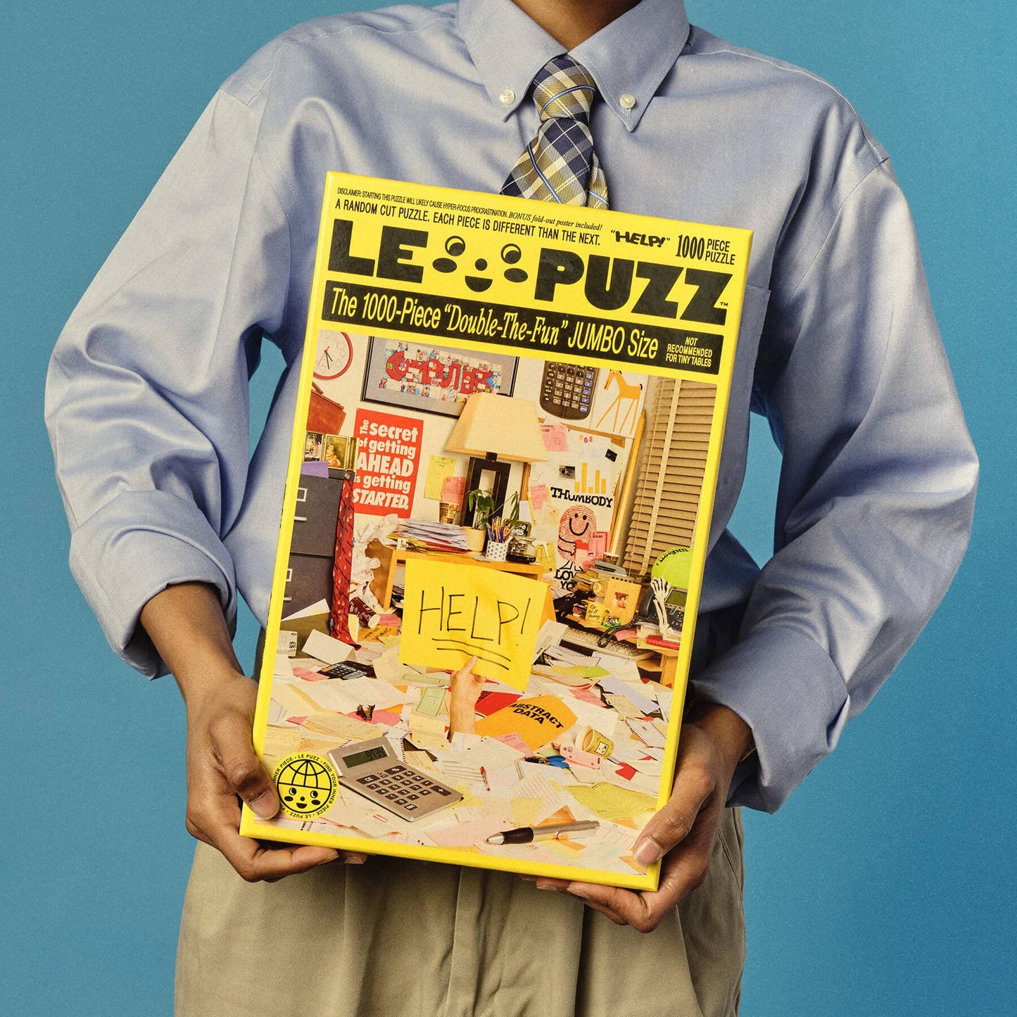 Person holding a large puzzle box titled 'LE PUZZ' against a blue background