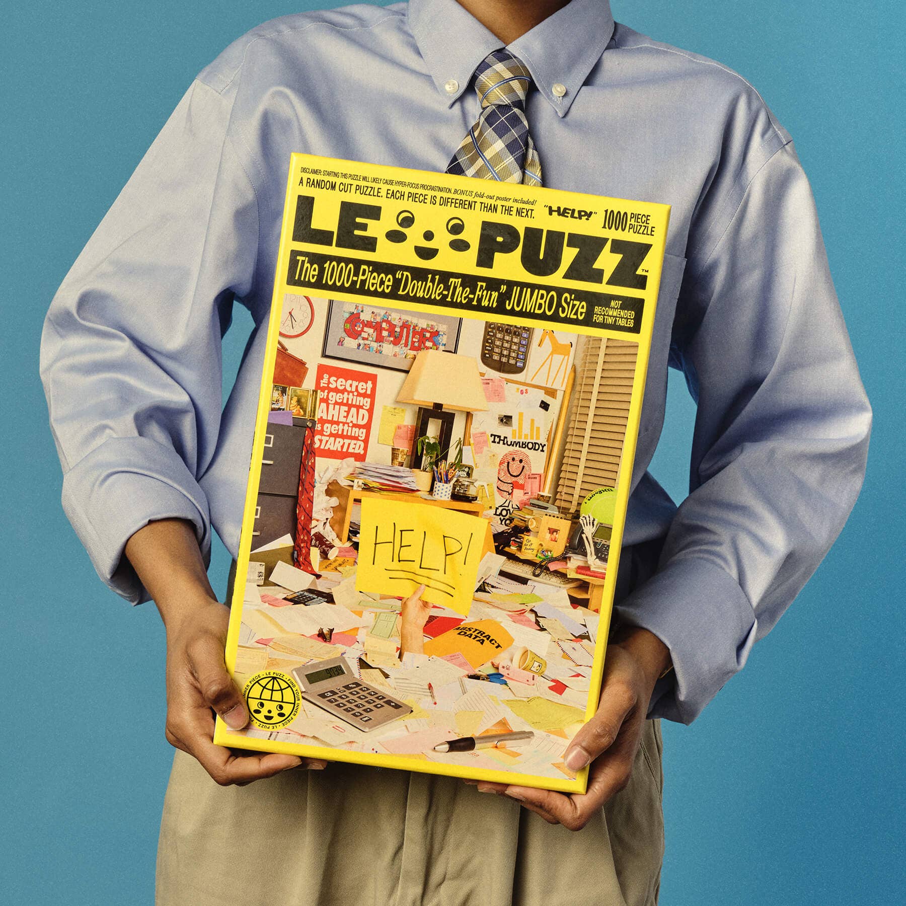 Person holding a large puzzle box titled 'LE PUZZ' against a blue background