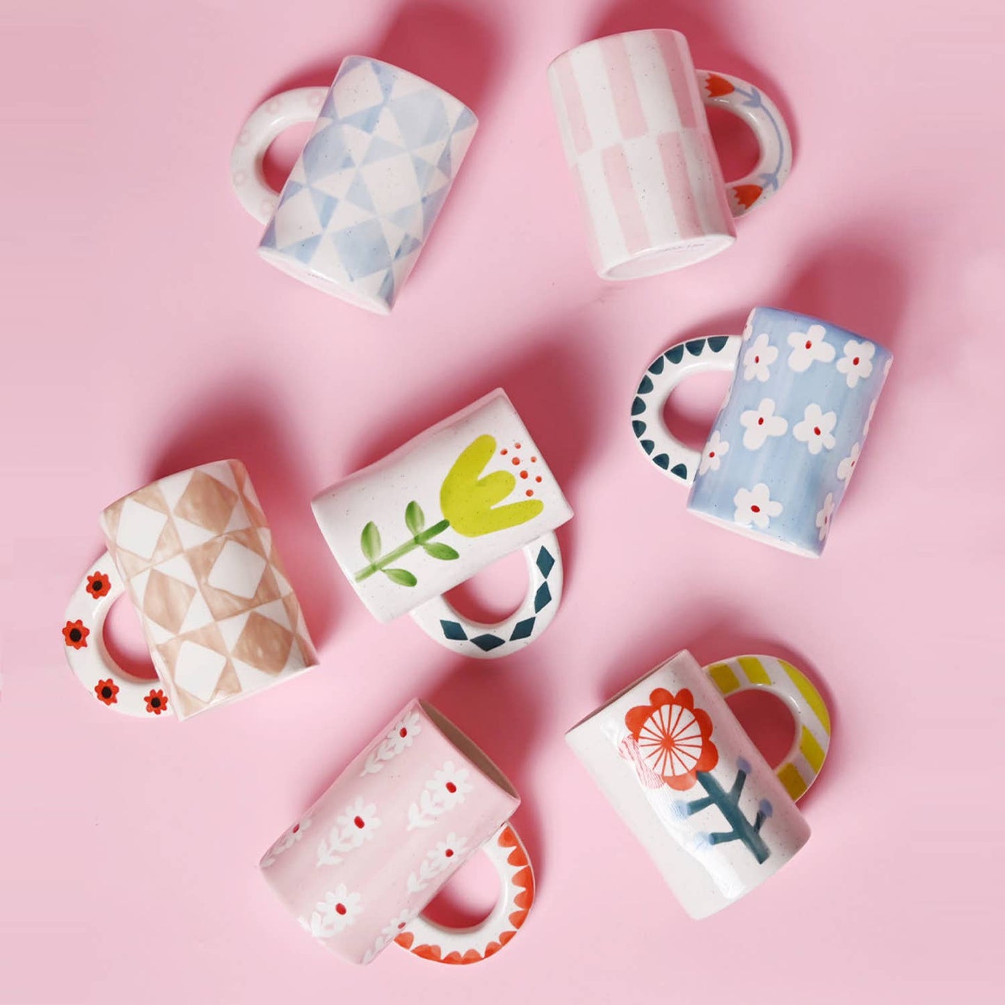 Set of colorful mugs with floral and geometric designs on a pink background
