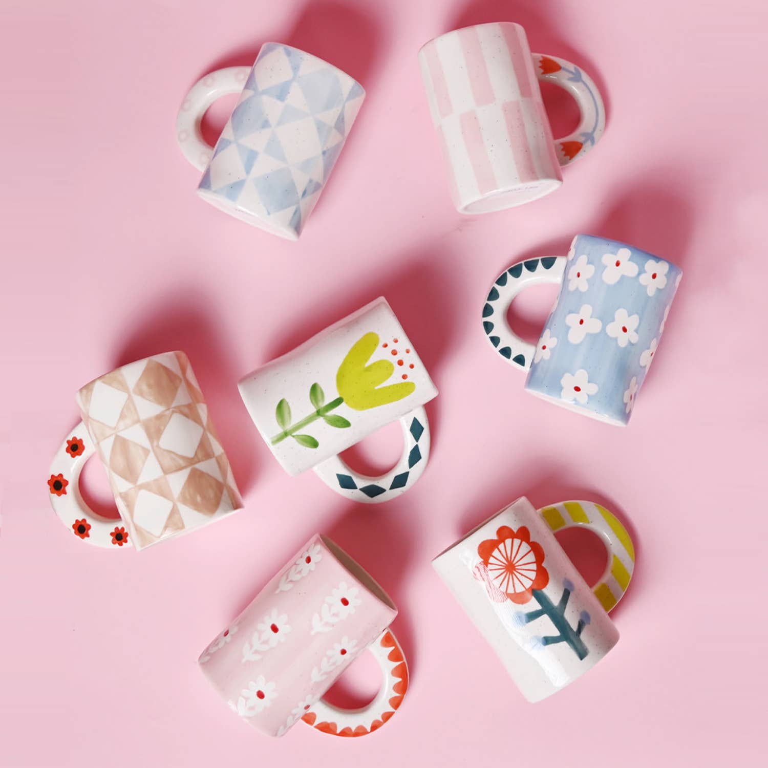 Set of colorful mugs with floral and geometric designs on a pink background