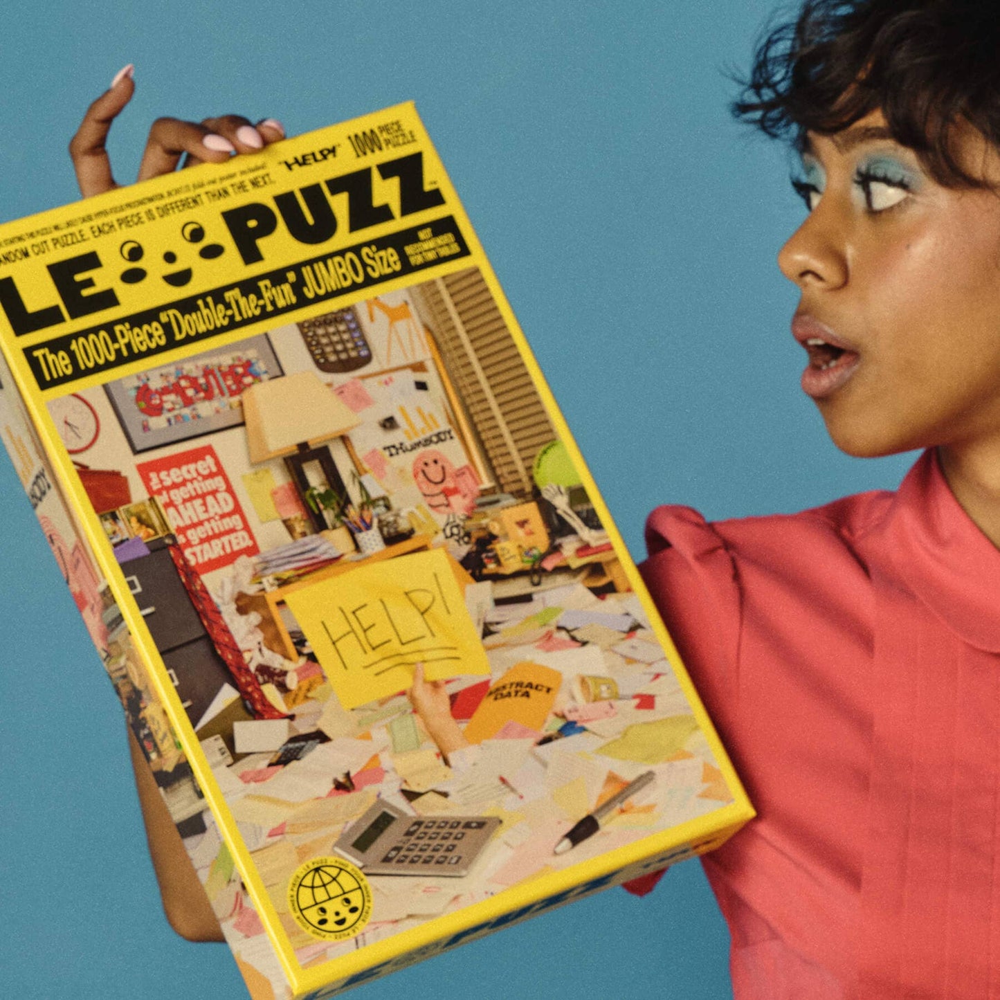 Person holding a large Le Puzz magazine with a colorful cover against a blue background