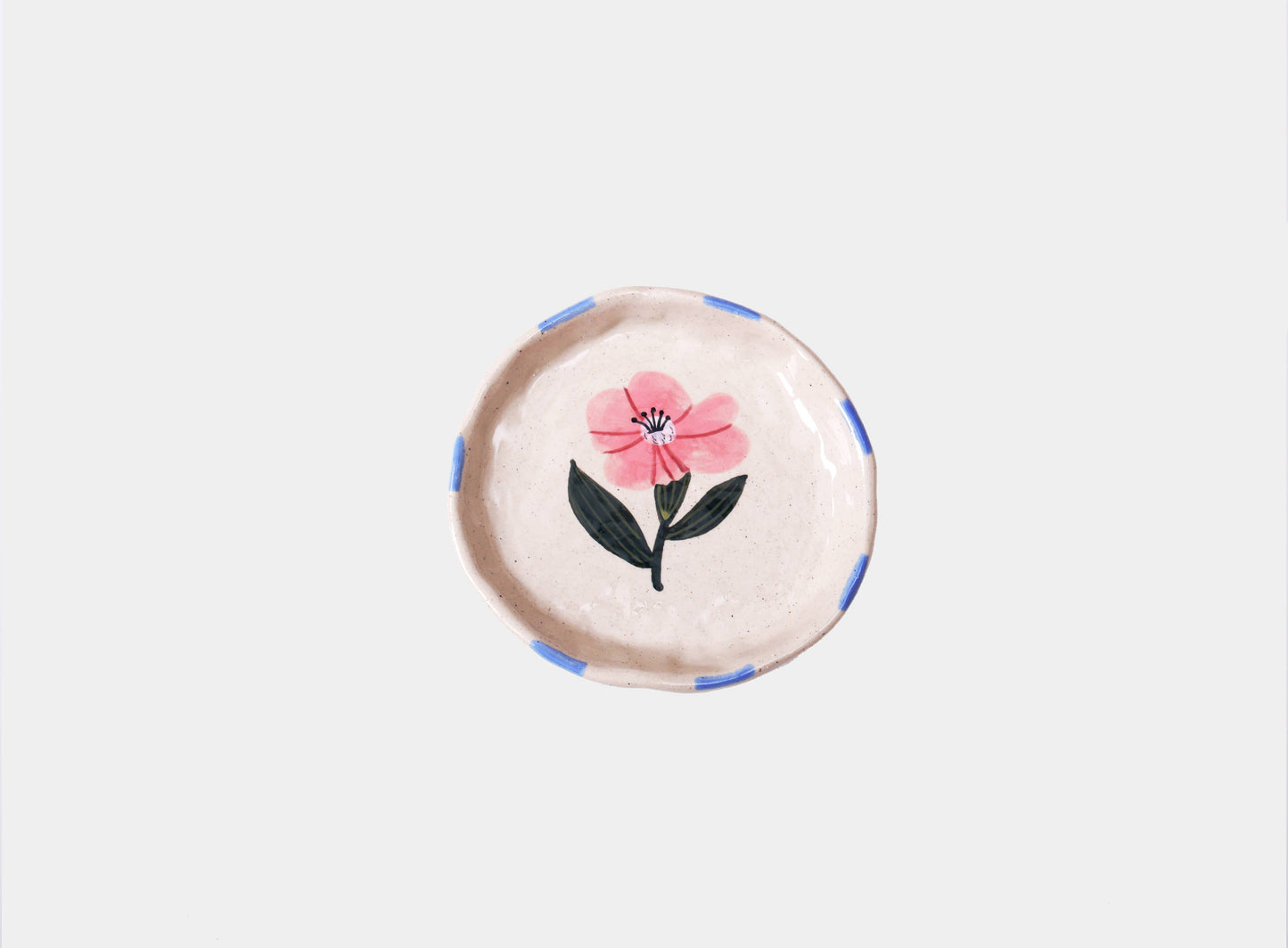 Round speckled cream stoneware trinket dish hand-painted with a single pink wild rose and green leaves, with blue dashes around the rim.