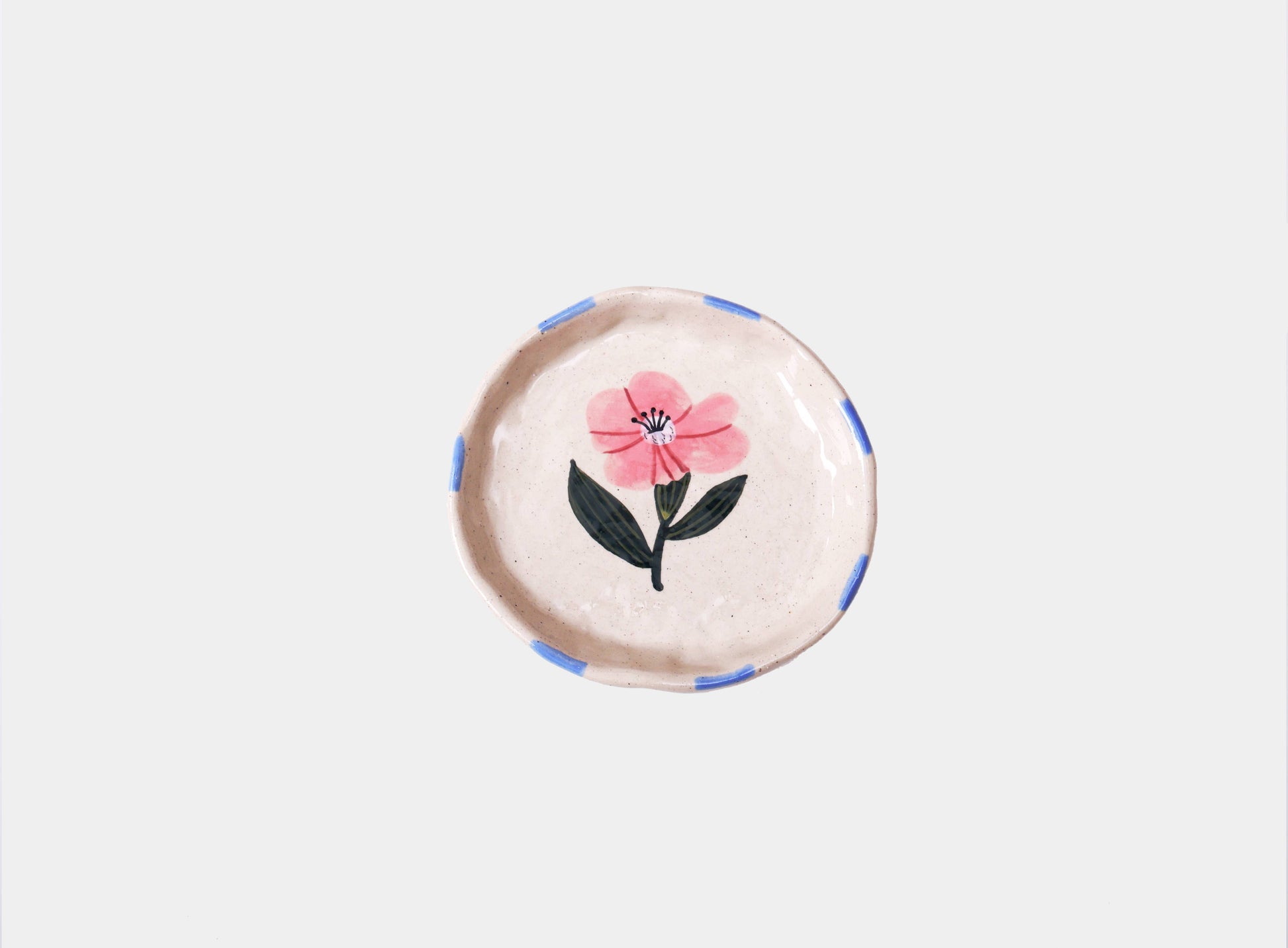 Round speckled cream stoneware trinket dish hand-painted with a single pink wild rose and green leaves, with blue dashes around the rim.