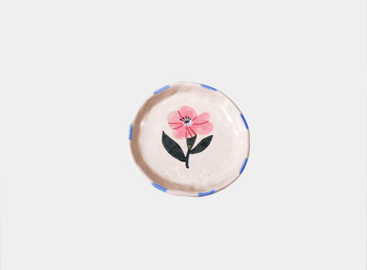 Round speckled cream stoneware trinket dish hand-painted with a single pink wild rose and green leaves, with blue dashes around the rim.
