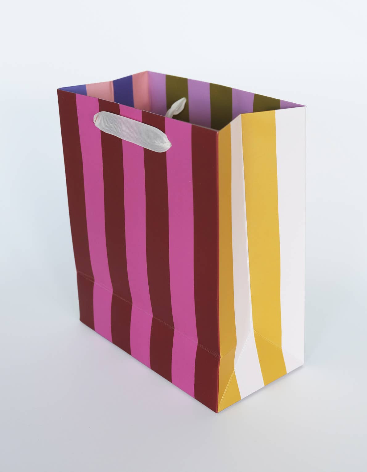 Colorful striped paper bag with a white handle on a light gray background