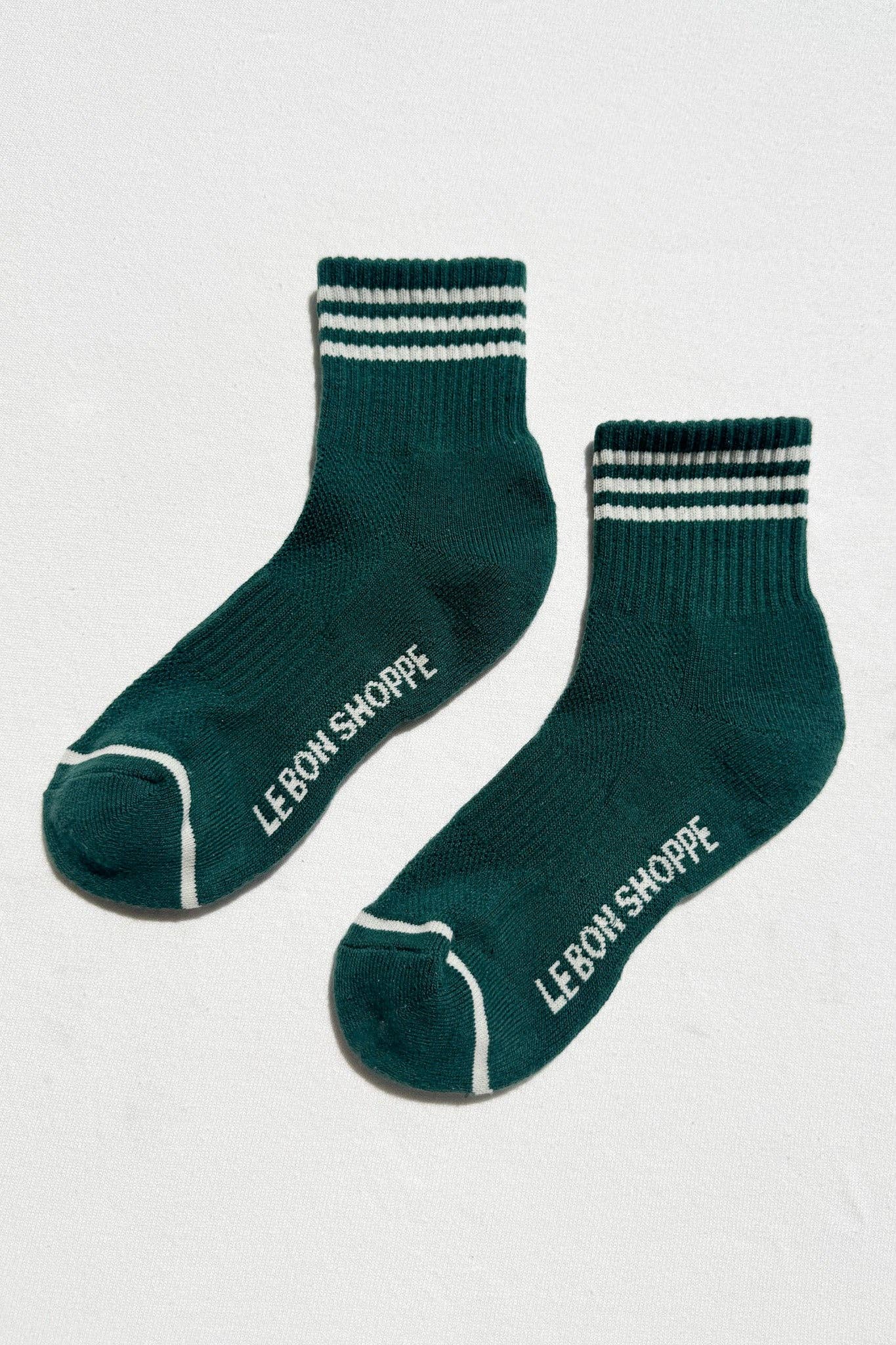 Pair of green socks with white stripes and 'Le Bon Shoppe' branding on a light gray background