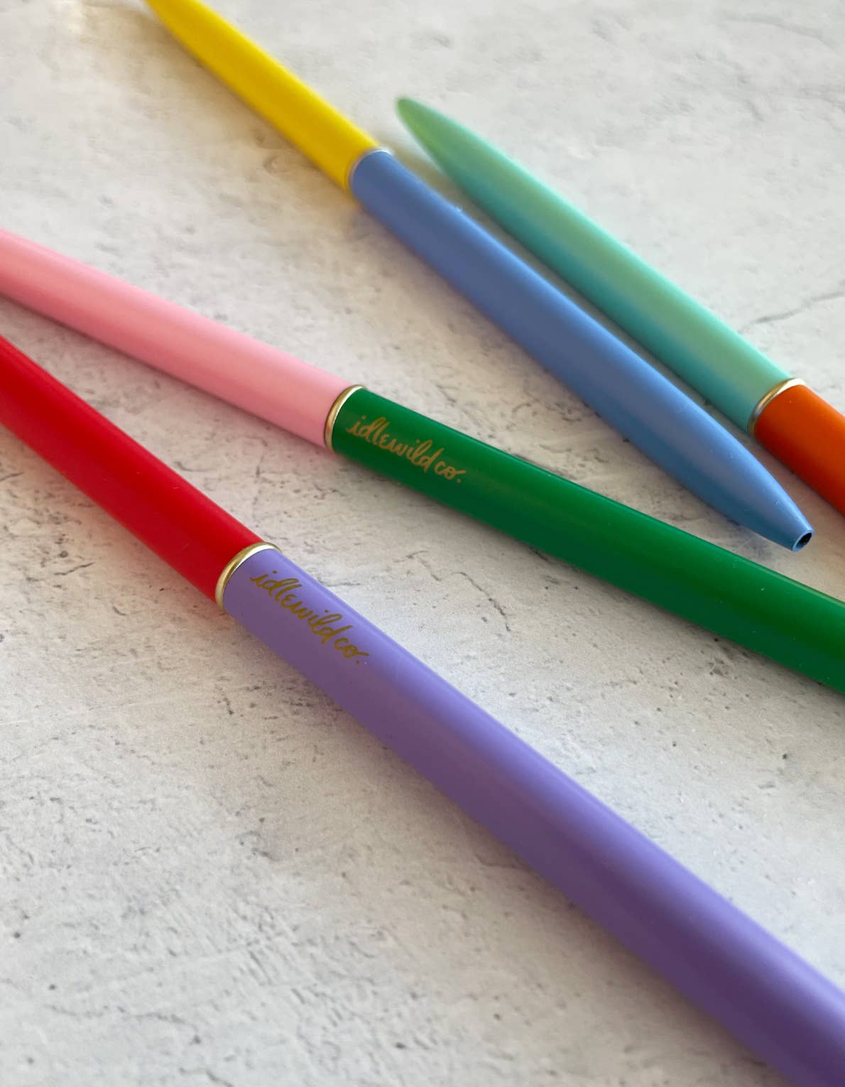 Colorful pens with visible brand name on a light textured surface
