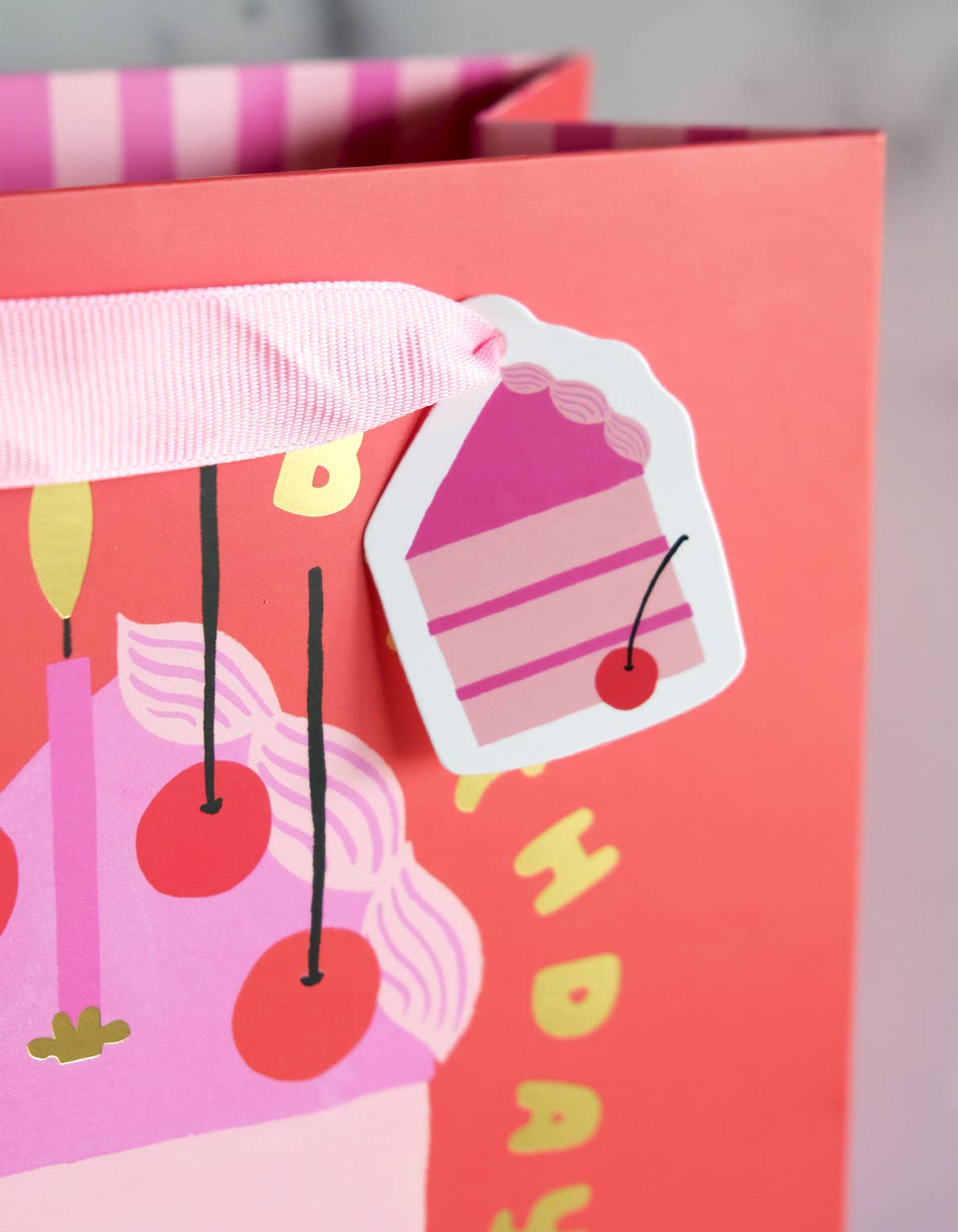 Gift bag with cake design and cherry on top, featuring a pink ribbon.